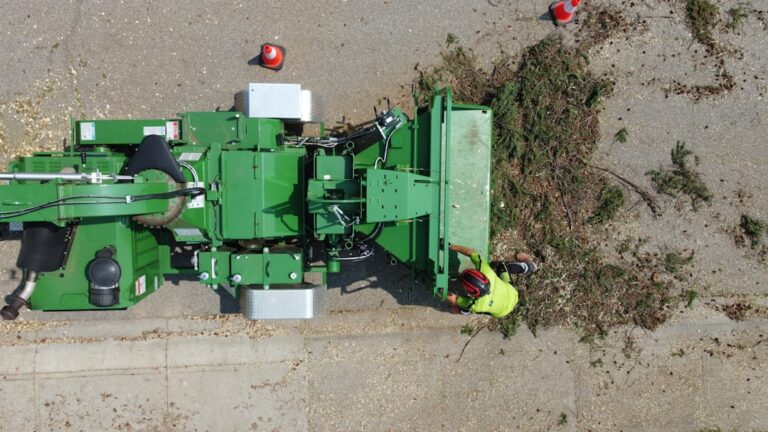 A person using a stump grinder to remove a tree stump in a grassy residential yard.